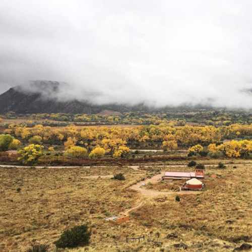 A scenic view of a valley with autumn trees, mountains in the background, and a small building amidst the landscape.