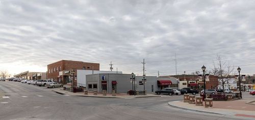 A small town street scene with shops, parked cars, and a cloudy sky.