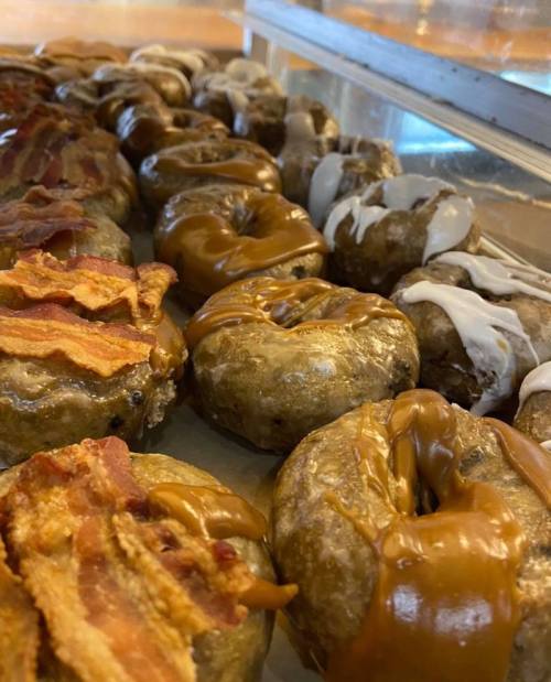 A close-up of assorted donuts topped with caramel, white icing, and crispy bacon.