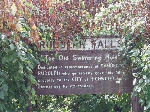 Sign for Rudolph Falls, dedicated to Samuel C. Rudolph, surrounded by greenery and leaves.