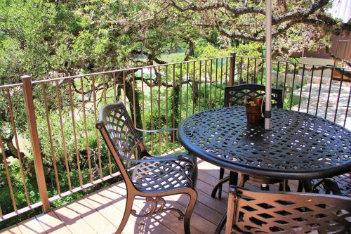 A patio with a round metal table and chairs, surrounded by greenery and a railing. Sunlight filters through the trees.
