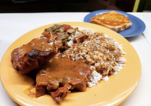 A plate of rice with brown gravy, two pieces of meat, mixed vegetables, and a slice of toasted bread on the side.