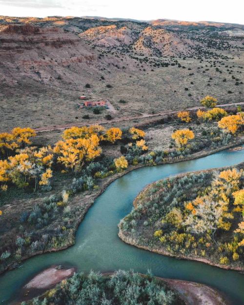 Aerial view of a winding river surrounded by autumn-colored trees and rugged hills in a serene landscape.