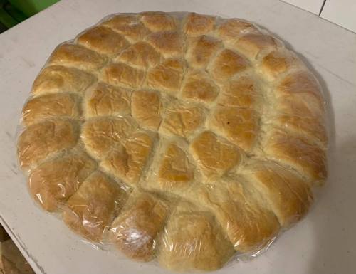 A round loaf of bread, partially covered in plastic wrap, with a golden-brown crust and soft texture.