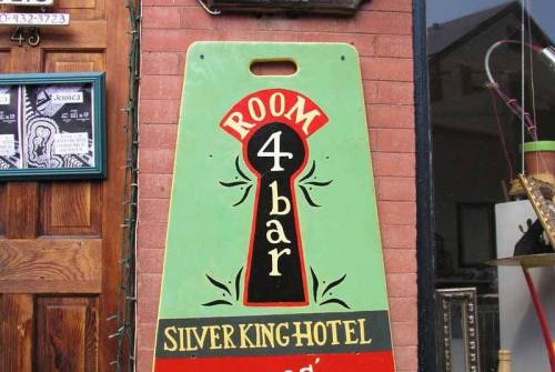 Sign for Silver King Hotel featuring "Room 4 Bar" in bold colors and a keyhole design.