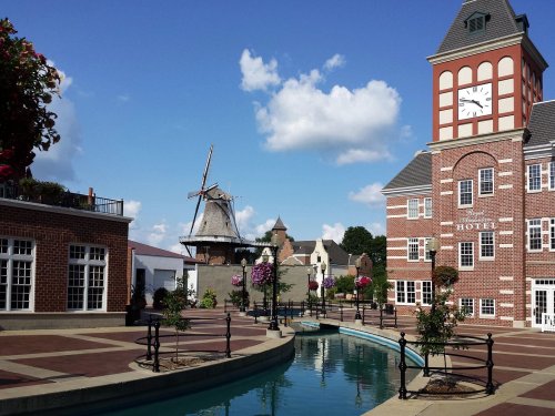 A charming town square featuring a hotel, a windmill, and a canal, with flowers and blue skies in the background.