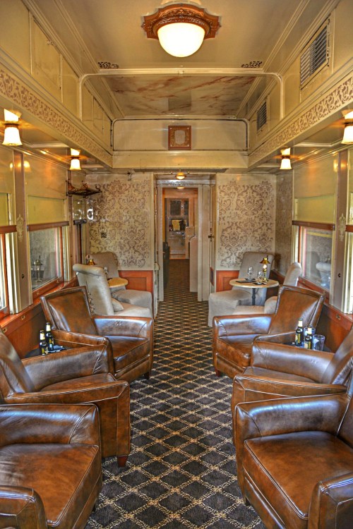 Interior of a vintage train car featuring leather armchairs, elegant decor, and a cozy atmosphere.