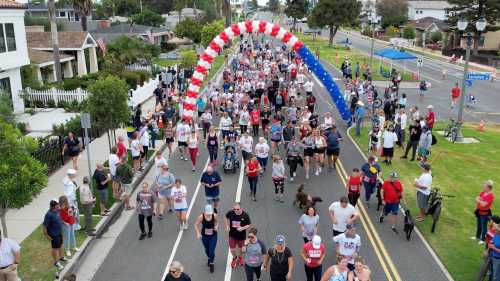 Aerial view of a large crowd participating in a festive run, with a colorful balloon arch and spectators along the route.