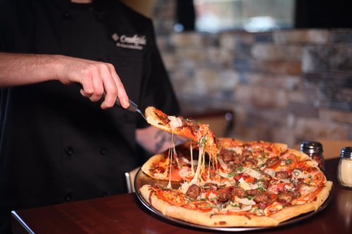A chef serving a cheesy, loaded pizza with various toppings from a wooden platter.