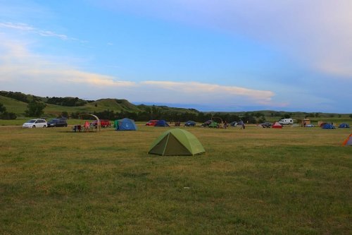 A grassy campsite with several tents and vehicles under a blue sky with scattered clouds.