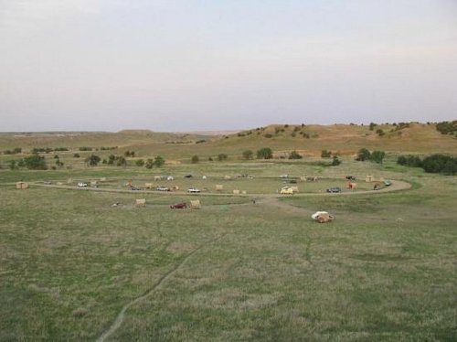 Aerial view of a circular campsite in a grassy landscape, surrounded by hills and sparse trees.