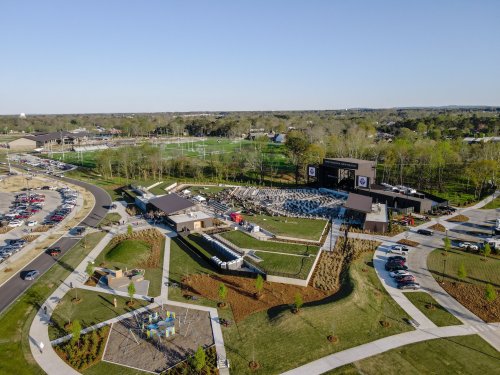 Aerial view of a large outdoor venue with a stage, seating area, and surrounding green spaces and parking.