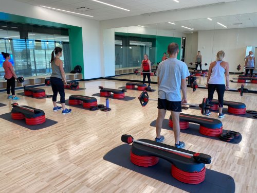 A group of people exercising in a gym studio with weights and benches, focused on their workout.