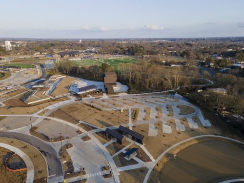 Aerial view of a park featuring pathways, a building, and sports fields in the background.