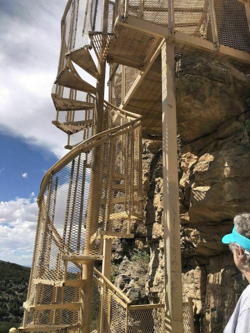 A spiral staircase made of metal, leading up a rocky cliff under a partly cloudy sky.