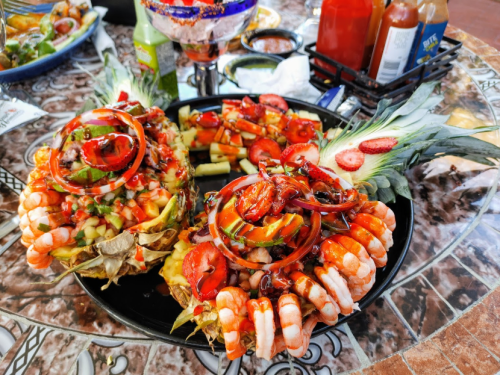 Two pineapple halves filled with shrimp, vegetables, and sauces, garnished with red onions and strawberries on a decorative plate.