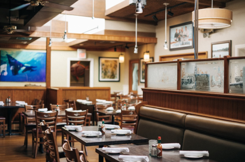 A spacious restaurant interior with wooden furniture, art on the walls, and neatly set tables.