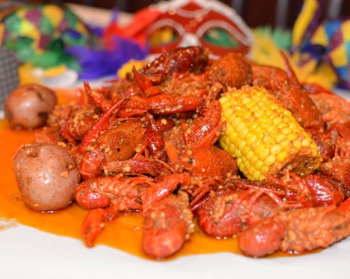 A vibrant platter of spicy crawfish, corn on the cob, and potatoes, surrounded by festive decorations.