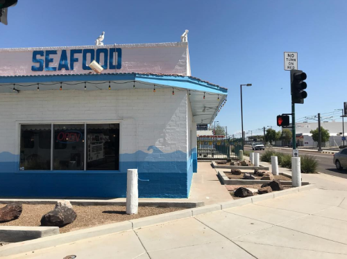 A seafood restaurant with an "OPEN" sign, blue trim, and a clear sky, located at a street corner with traffic lights.