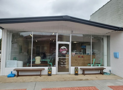 Exterior of a modern café with large windows, benches, and a sign that reads "Olivia's." Cloudy sky in the background.