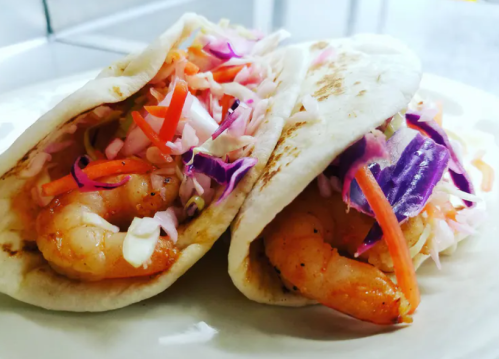 Two shrimp tacos filled with colorful slaw, served in soft tortillas on a white plate.