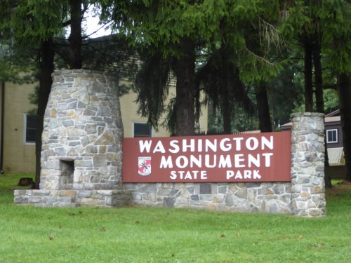 Sign for Washington Monument State Park, featuring a stone structure and surrounded by trees.