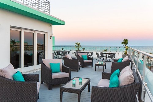 Rooftop terrace with cozy seating, tables, and ocean view at sunset, featuring teal cushions and candles.