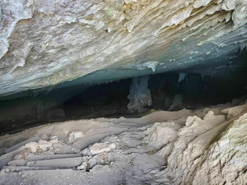 A dimly lit cave interior with rocky formations and stalactites hanging from the ceiling.