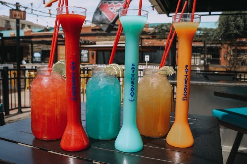 Colorful cocktails in tall glasses with straws, featuring vibrant red, blue, orange, and yellow drinks on a table.