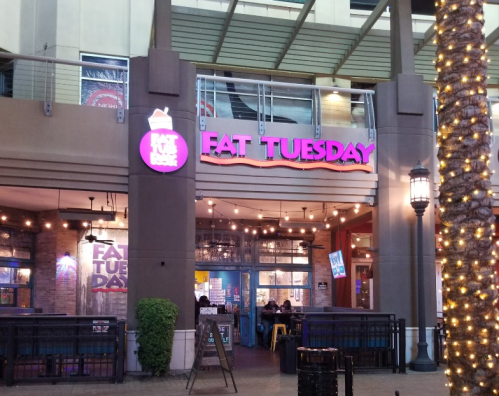 Exterior of a restaurant named "Fat Tuesday," featuring bright signage and outdoor seating.