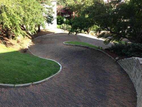 A winding cobblestone path surrounded by greenery and trees, leading through a landscaped area.