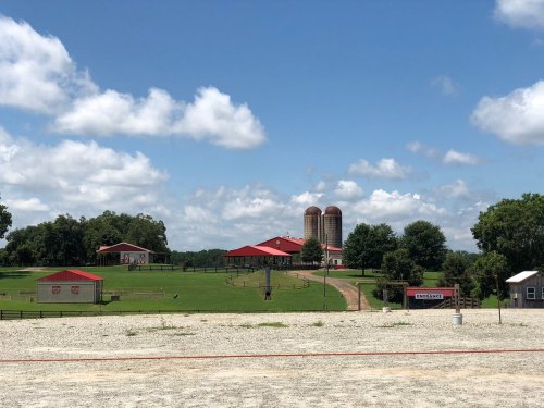 A scenic farm with red-roofed buildings, silos, and green fields under a blue sky with fluffy clouds.