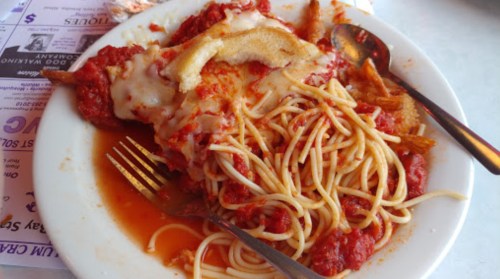 A plate of spaghetti with marinara sauce and cheese, alongside a piece of breaded meat, partially eaten with utensils.