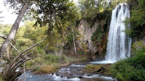 A serene waterfall cascading down rocky cliffs, surrounded by lush greenery and a flowing river below.