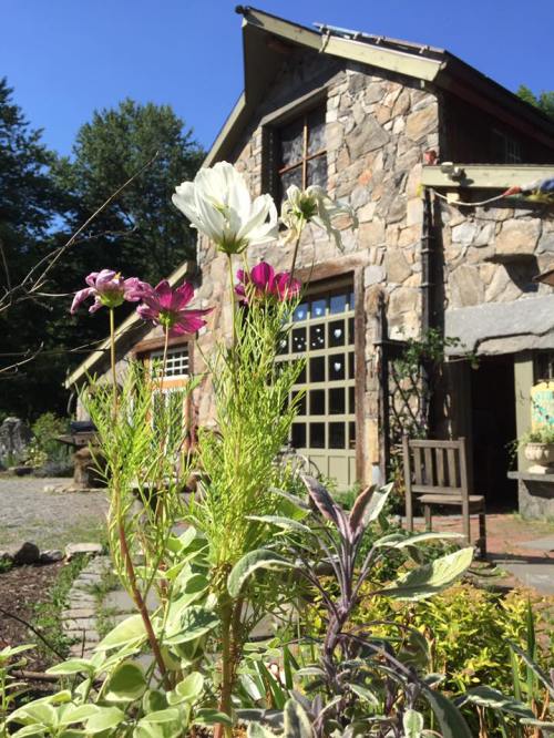 A stone house surrounded by colorful flowers and greenery under a clear blue sky.