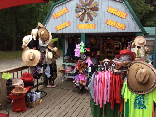 A colorful outdoor shop displaying hats, t-shirts, sunglasses, and souvenirs on a wooden deck.