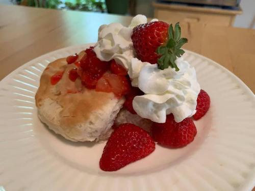 A plate of strawberry shortcake topped with whipped cream and fresh strawberries on a wooden table.