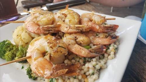 Grilled shrimp skewers served on a bed of couscous with broccoli and cauliflower.