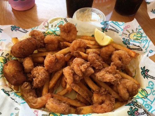 A basket of crispy fried shrimp and French fries, garnished with a lime wedge and served with dipping sauce.