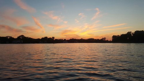 A serene sunset over a calm lake, with colorful clouds reflecting on the water's surface.