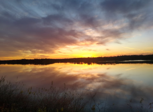 A serene sunset over a calm lake, with vibrant colors reflecting on the water and clouds in the sky.