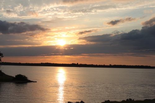 Sunset over a calm lake, with clouds reflecting warm colors in the sky and a shimmering path of light on the water.