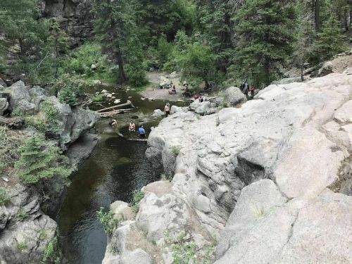 A rocky landscape with a small river, surrounded by trees, where people are enjoying the water and nature.