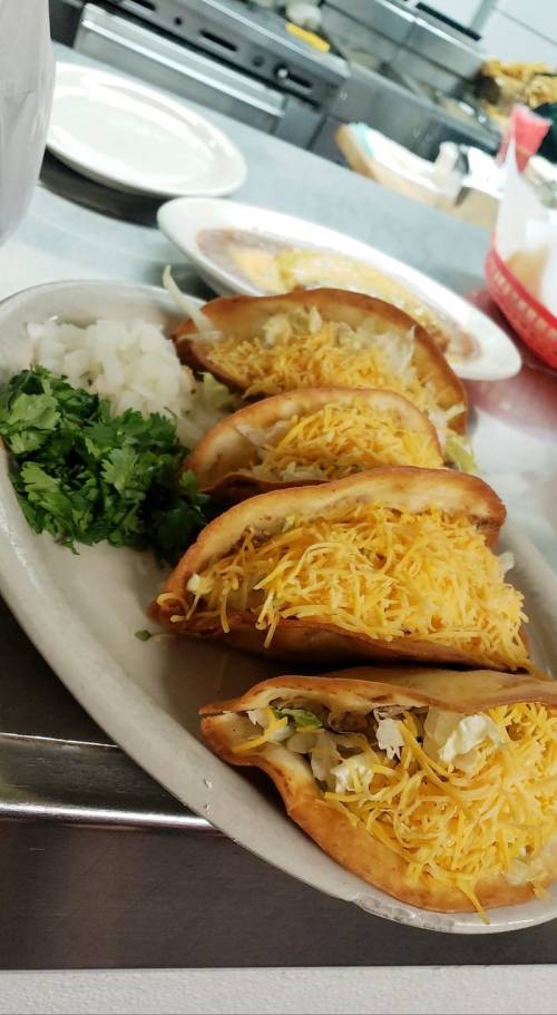 A plate of crispy tacos filled with cheese, served with chopped onions and cilantro on the side.
