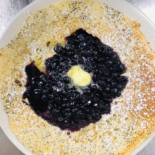A large pancake topped with blueberries, a dollop of butter, and a dusting of powdered sugar.