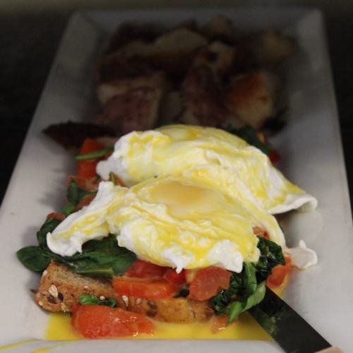 A plate featuring poached eggs on toast with spinach and tomatoes, accompanied by roasted potatoes.