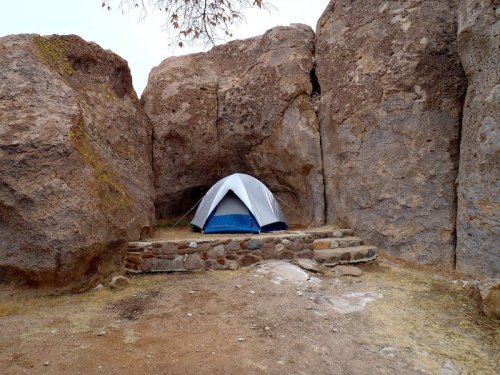 A small blue and white tent set between two large rocky formations in a natural outdoor setting.