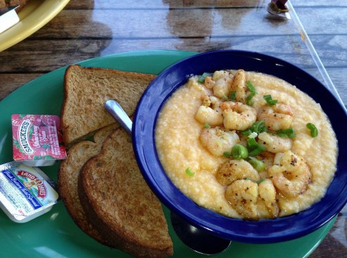 A bowl of shrimp and grits served with two slices of toast and condiments on a green plate.