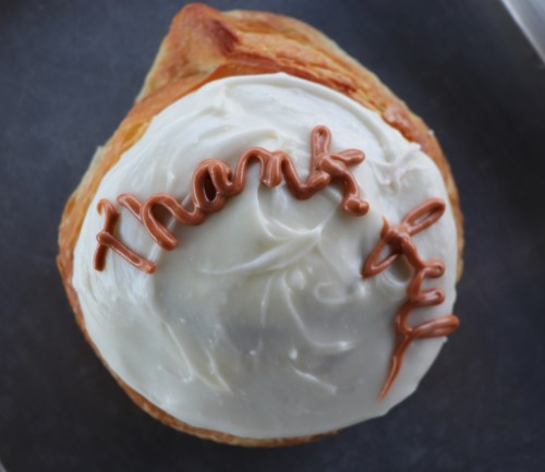 A pastry topped with white frosting and the word "thankful" written in brown icing.