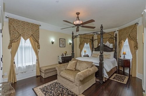 Elegant bedroom featuring a four-poster bed, cozy seating area, and rich drapery in warm tones.